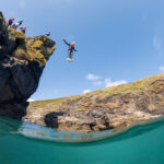 Cliff jumper mid-air at Praa Sands with Kernow Coasteering – a favourite coasteering spot in south Cornwall.