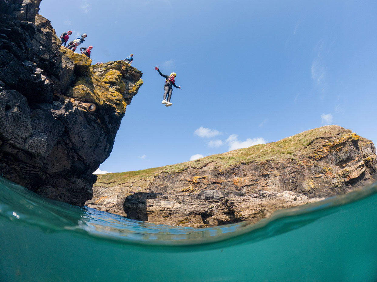 Cliff jumper mid-air at Praa Sands with Kernow Coasteering – a favourite coasteering spot in south Cornwall.