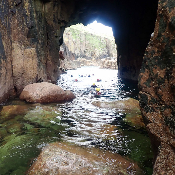 Coasteering group swims through the massive Gamper Hole arch before the final climb at Land’s End