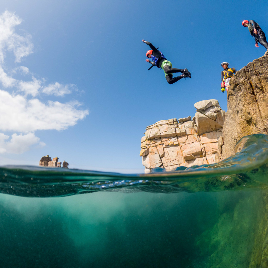 Group jumping into the sea near Porthleven on Cornwall’s coast – a fun outdoor experience for visitors staying in Hayle Cornwall or looking for things to do near St Ives
