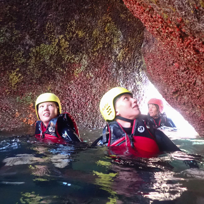 Coasteering group exploring a colourful grotto beneath granite boulders on St. Mary’s, Isles of Scilly