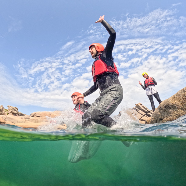 Friends jumping together into the sea during a coastal adventure on the Scillies