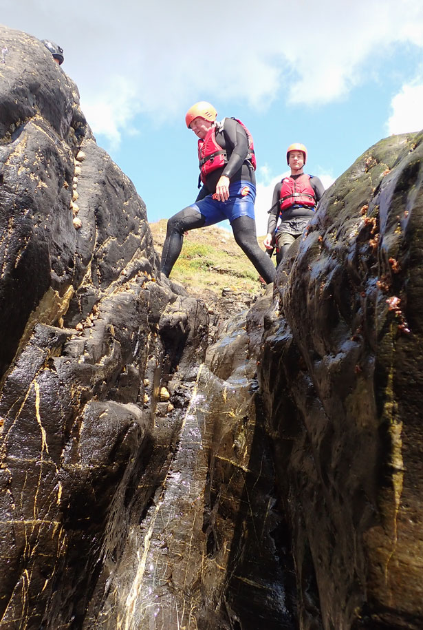 Man stepping across a narrow gully on Cornwall’s rugged coast during a beginner session