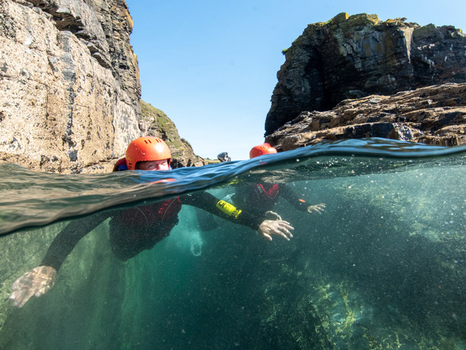Group swimming through a dramatic coastal gully on a beginner family adventure in Cornwall