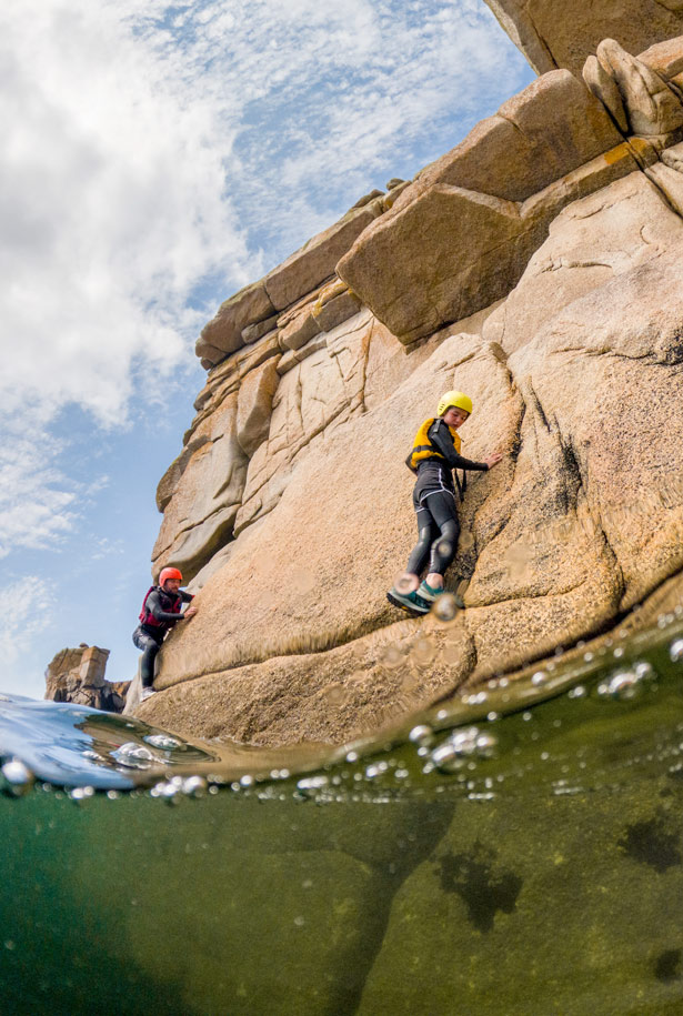Young girl climbing a granite rock face with clear ocean waters beneath, exploring the rugged coastline near Hugh Town, Isles of Scilly.
