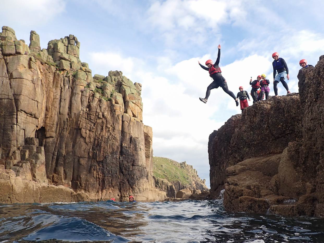 Group coasteering near Land’s End, leaping from a rocky ledge into Atlantic swell