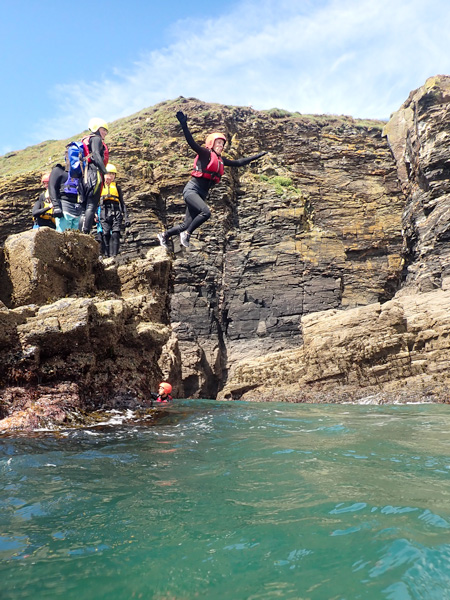 Child jumps into the sea with family watching from the rocks — a fun thing to do with kids in Cornwall.