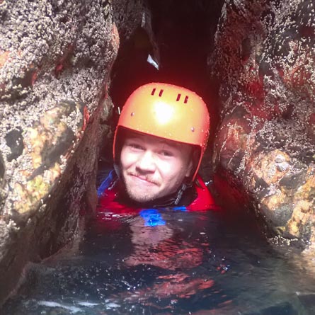 What to wear for coasteering: participant wearing a wetsuit, helmet, buoyancy aid, and trainers to explore the coast