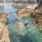 Family group explores rock formations at low tide near Penzance on a guided coasteering route