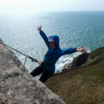 Beginner abseiler descending a sea cliff in Cornwall with scenic ocean backdrop