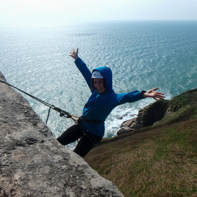 Beginner abseiler descending a sea cliff in Cornwall with scenic ocean backdrop
