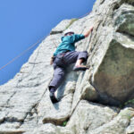 Beginner climber ascending granite face at Trewavas Head in Cornwall