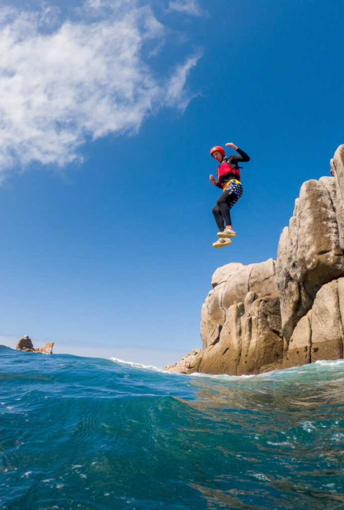 Person coasteering off granite cliffs into the sea on the Cornish coast – one of the top things to do in Cornwall