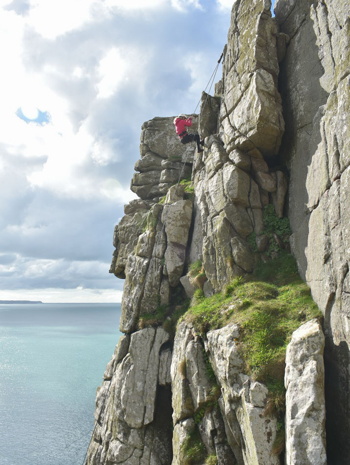Girl top-roping near the top of a broad sea cliff on Cornwall’s south coast