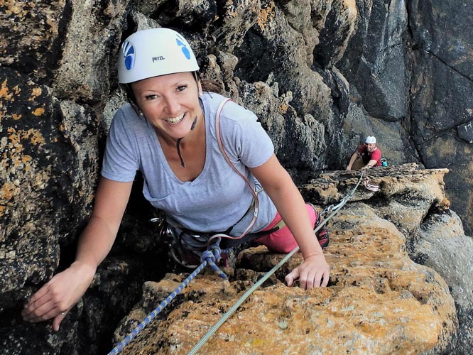 Smiling woman seconding a beginner-friendly trad route at Sennen Cove.