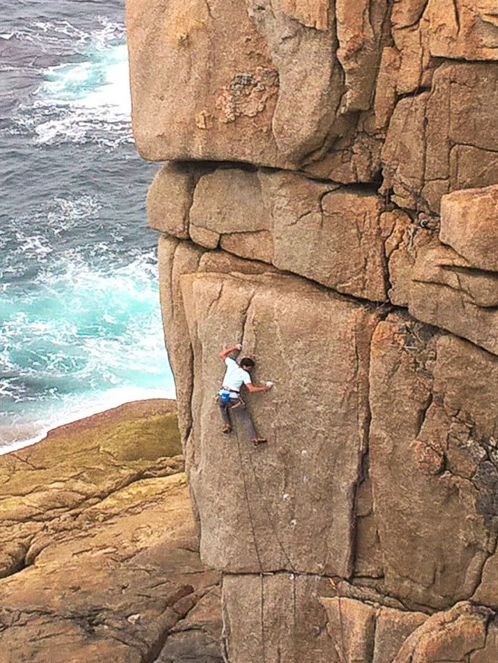 Lead climber committing to the steep crux of Demolition (E6) at Sennen, with the Atlantic just below.