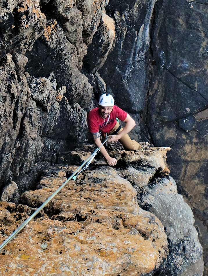 A beginner climber seconding Staircase at Sennen — an ideal first trad route on real Cornish granite.