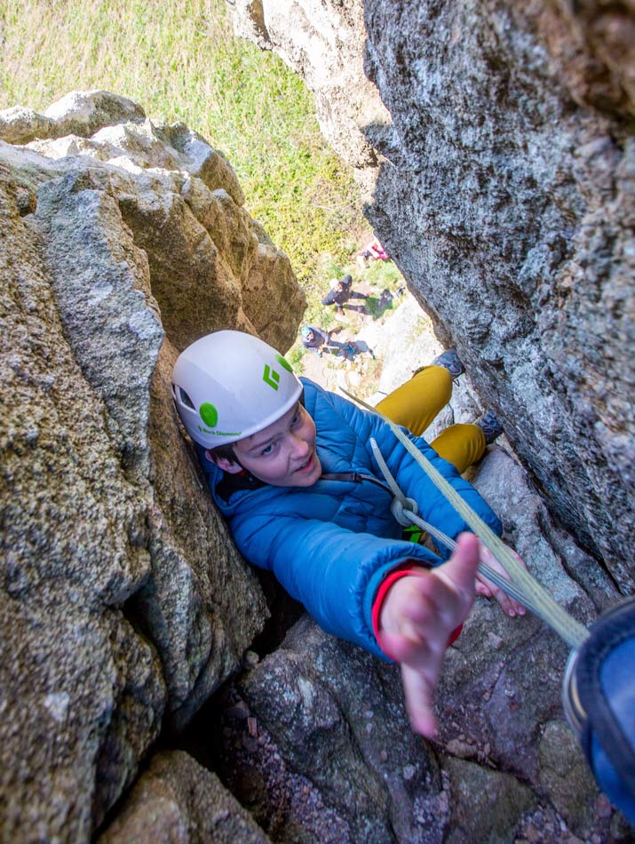 Boy stretching for the anchor chains on a chimney climb in Cornwall