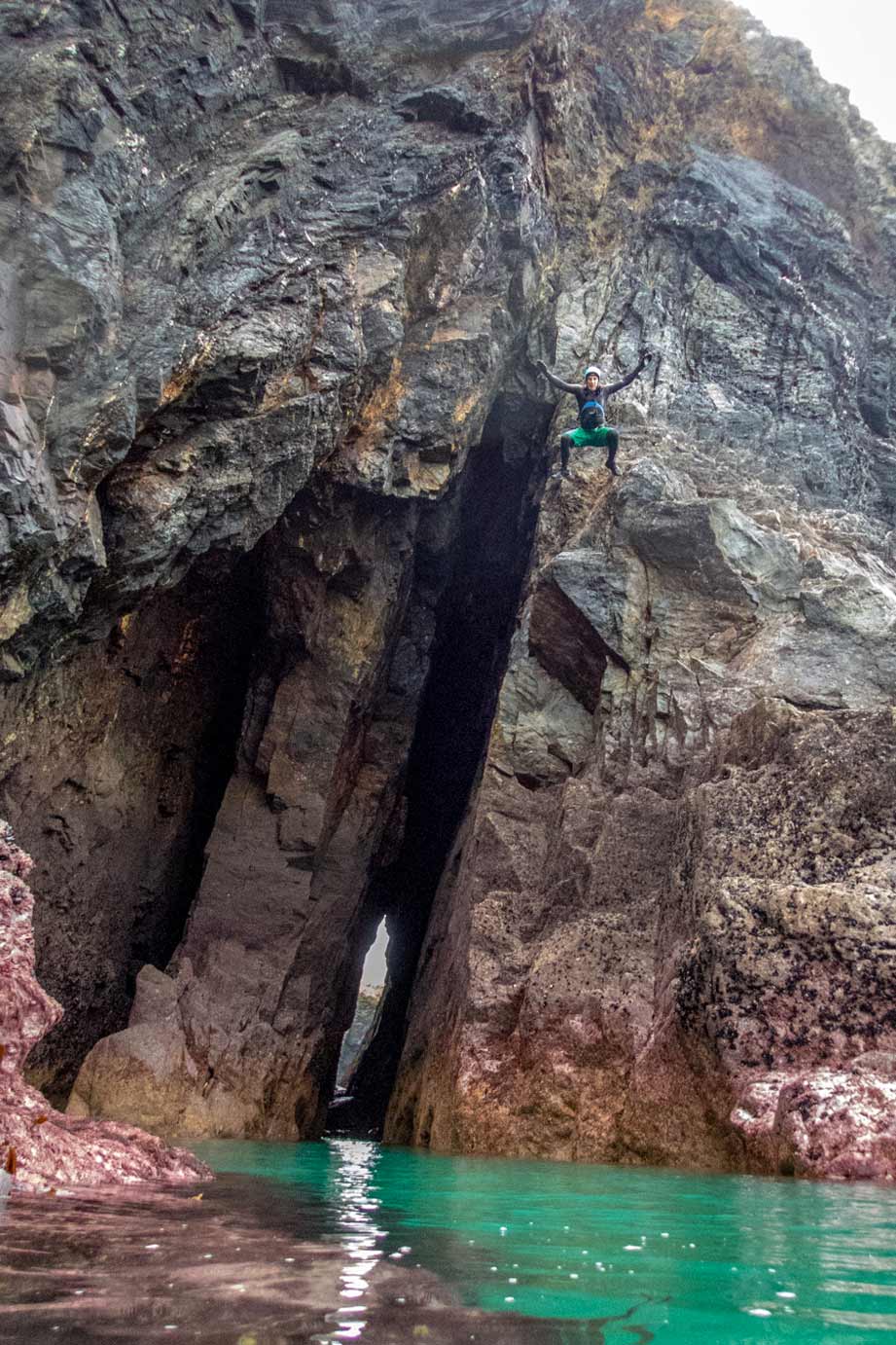 Coasteering guide jumping across a double sea arch on Cornwall’s remote coastline