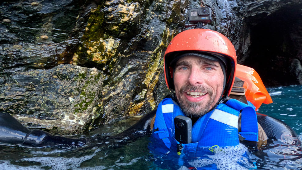 Coasteering guide in helmet and buoyancy aid emerges from a deep sea cave on the Cornwall coast