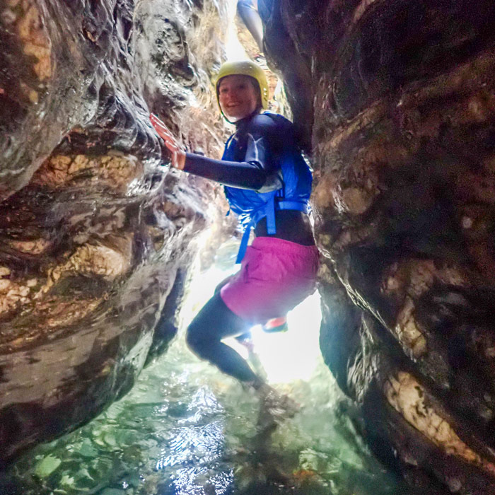 Sapphire, coasteering guide, squeezing through a narrow coastal chasm during an adventurous guided session in Cornwall.