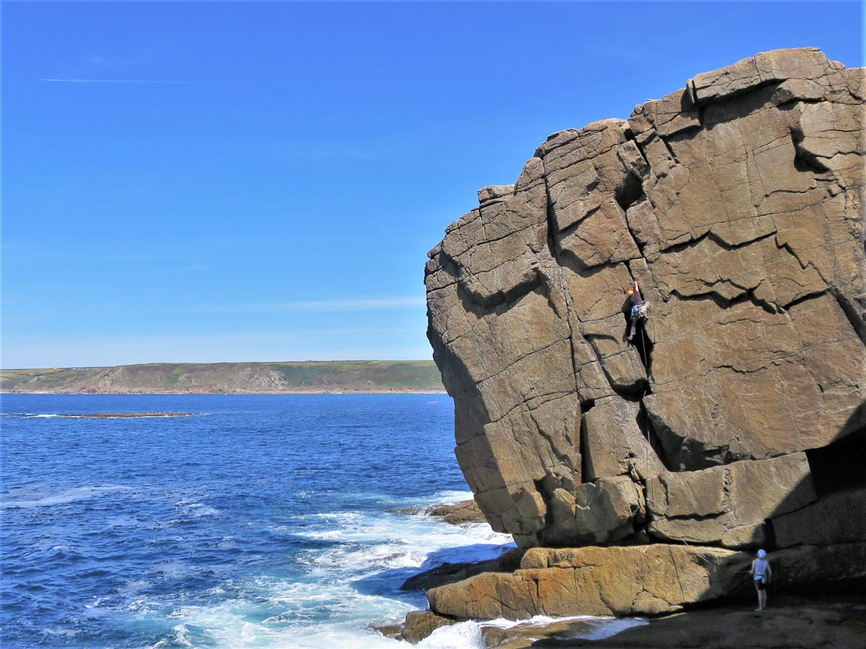 Climber tackling Zig Zag, a classic HVS trad route at Black Zawn, with Sennen Cove and Gwenver beach in the background.