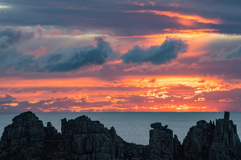 Fiery dawn sky above Logan Rock near Treen, West Cornwall