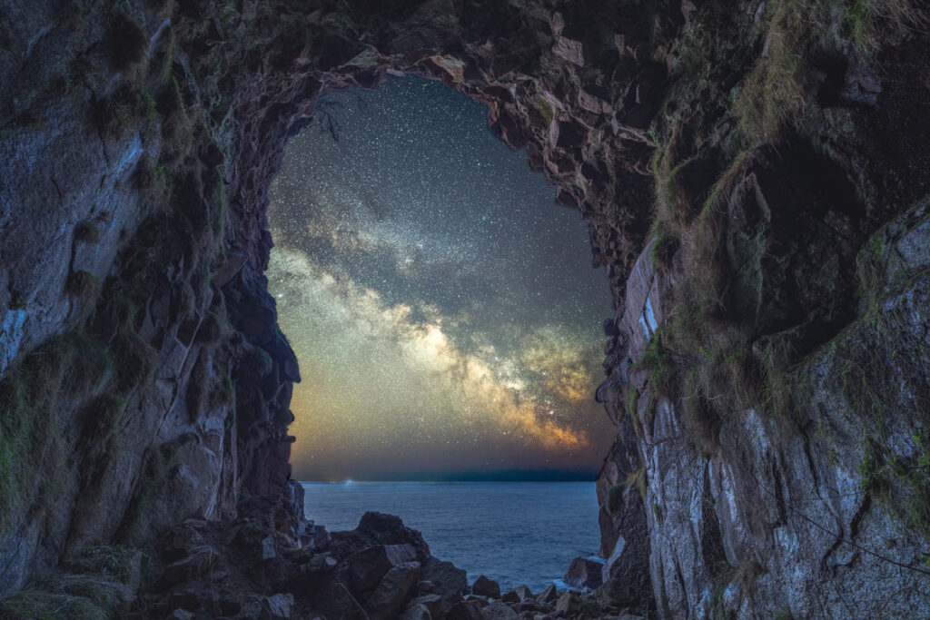 Milky Way framed by the dark rock walls of Mousehole Cave, Cornwall