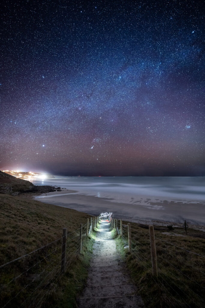 Winter Milky Way and Orion over light trails on the path to Gwynver Beach, Cornwall