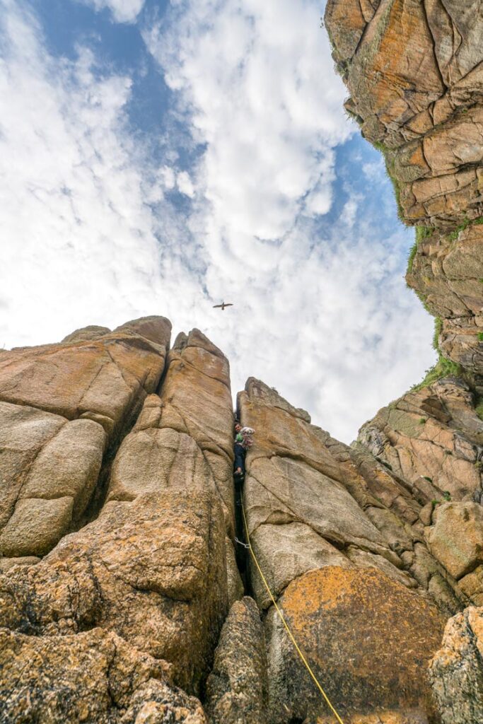 Climber ascending the off-width crack of Suamico (E3) at Green Bay, Porthcurno, Cornwall