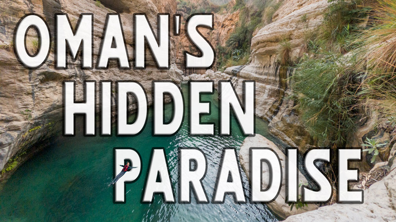 A person floats in a turquoise wadi pool beneath sculpted canyon walls in Wadi Mibam, Oman