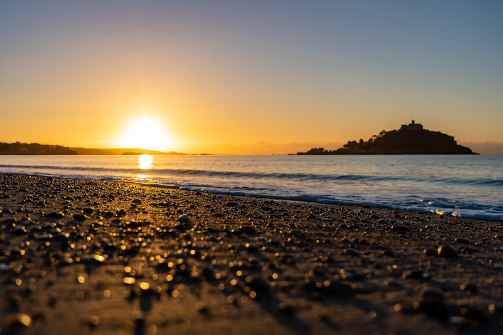 Sunrise at St Michael’s Mount, with warm bokeh foreground and pebbled beach